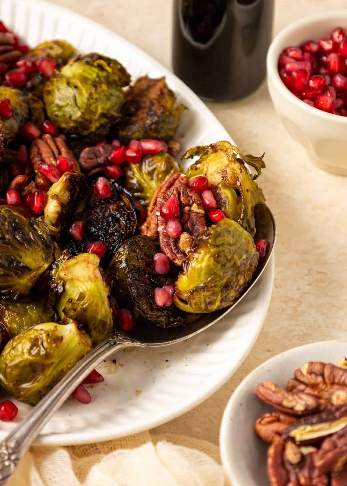 Balsamic Brussels sprouts roasted with pecans and pomegranate seeds on a white plate.