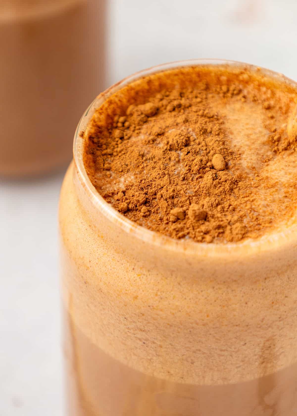A glass of frothy Chocolate Protein Shake topped with a layer of cocoa powder.