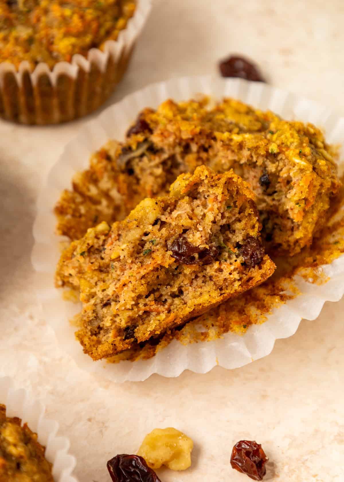 A sliced Superhero Muffin with raisins and nuts on a white liner, muffin in background.