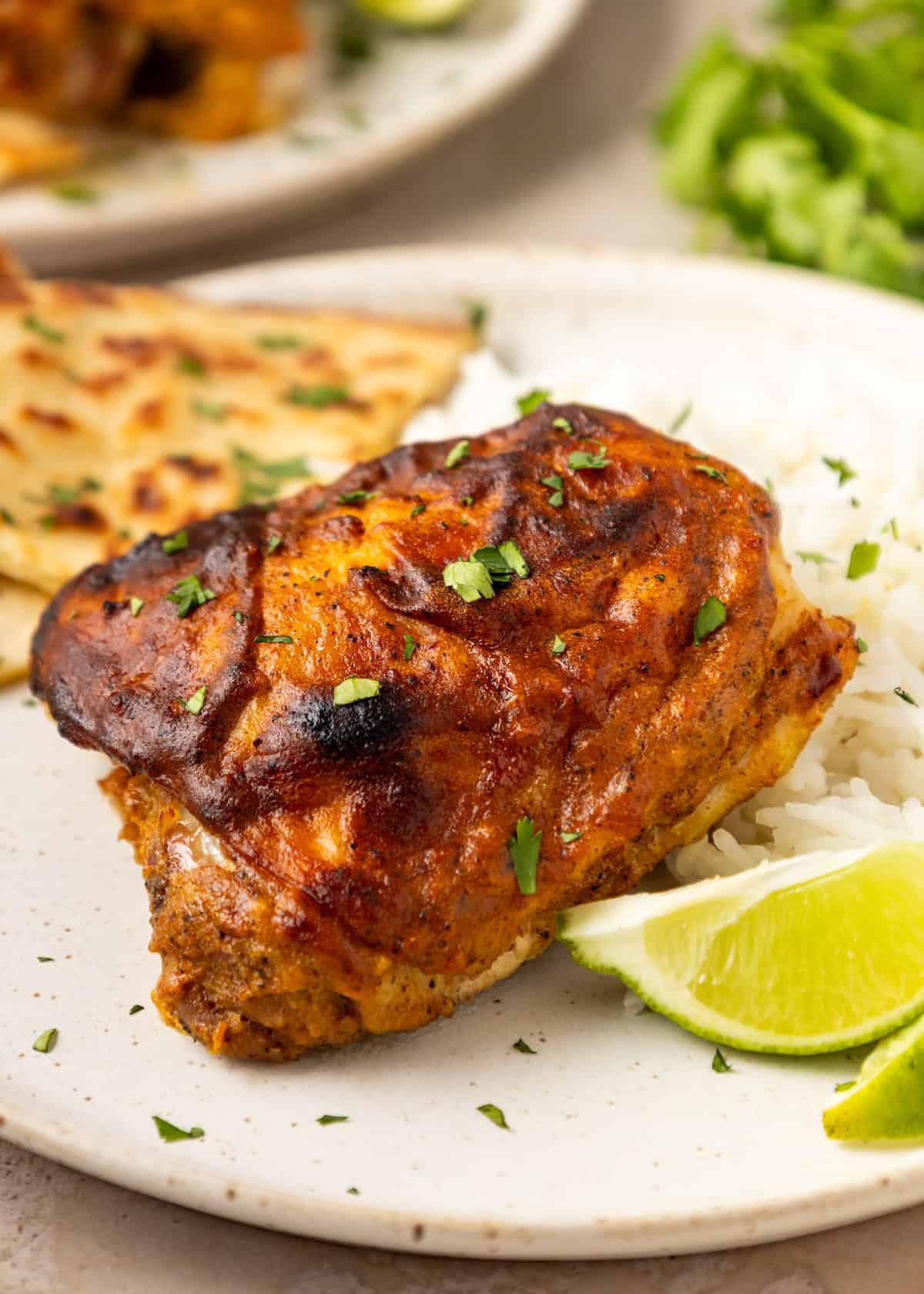 Tandoori Chicken with rice, naan, lime wedges, and herbs on a white plate.