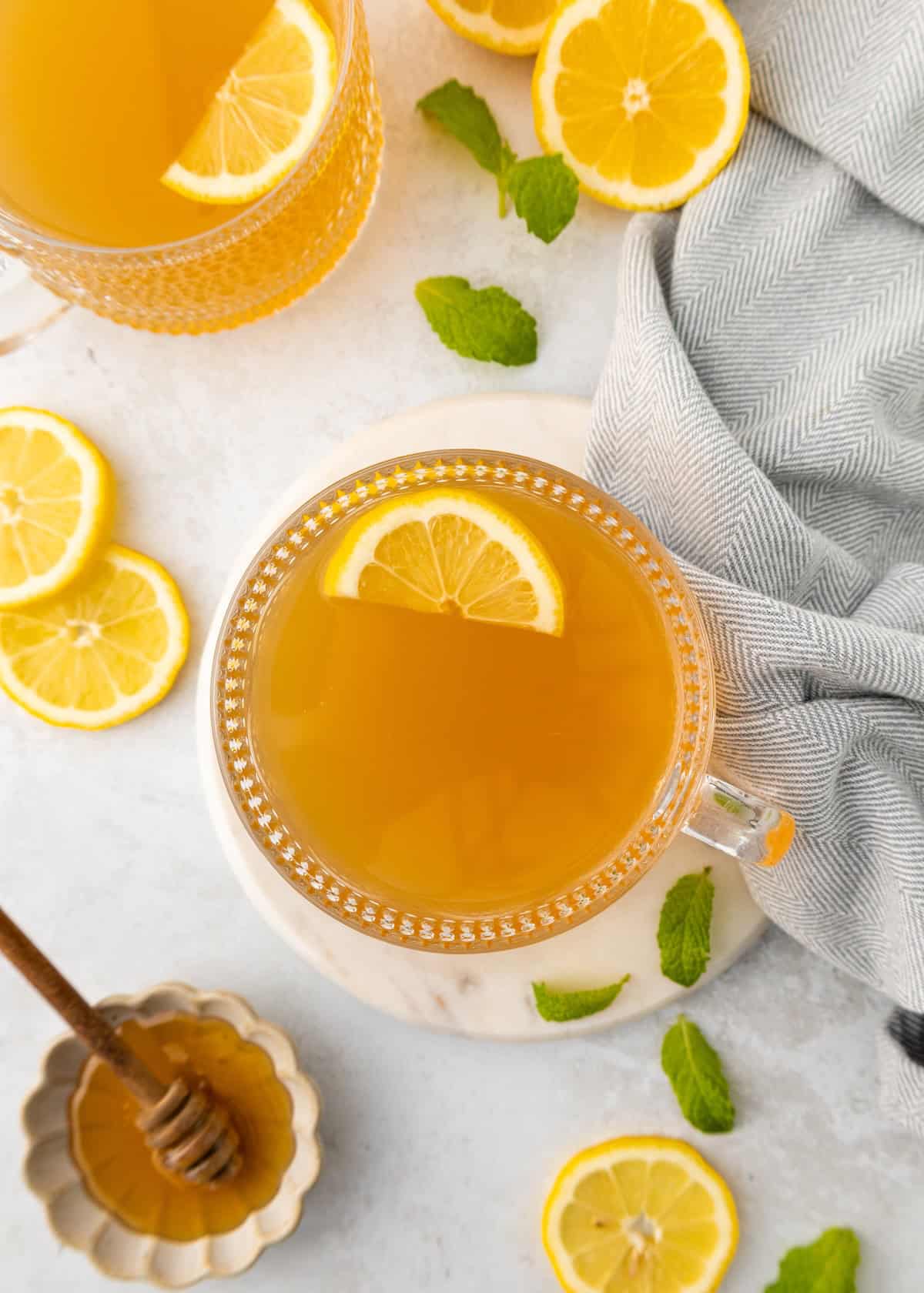 A cup of Medicine Ball Tea with a lemon slice, mint leaves, and a honey dipper.