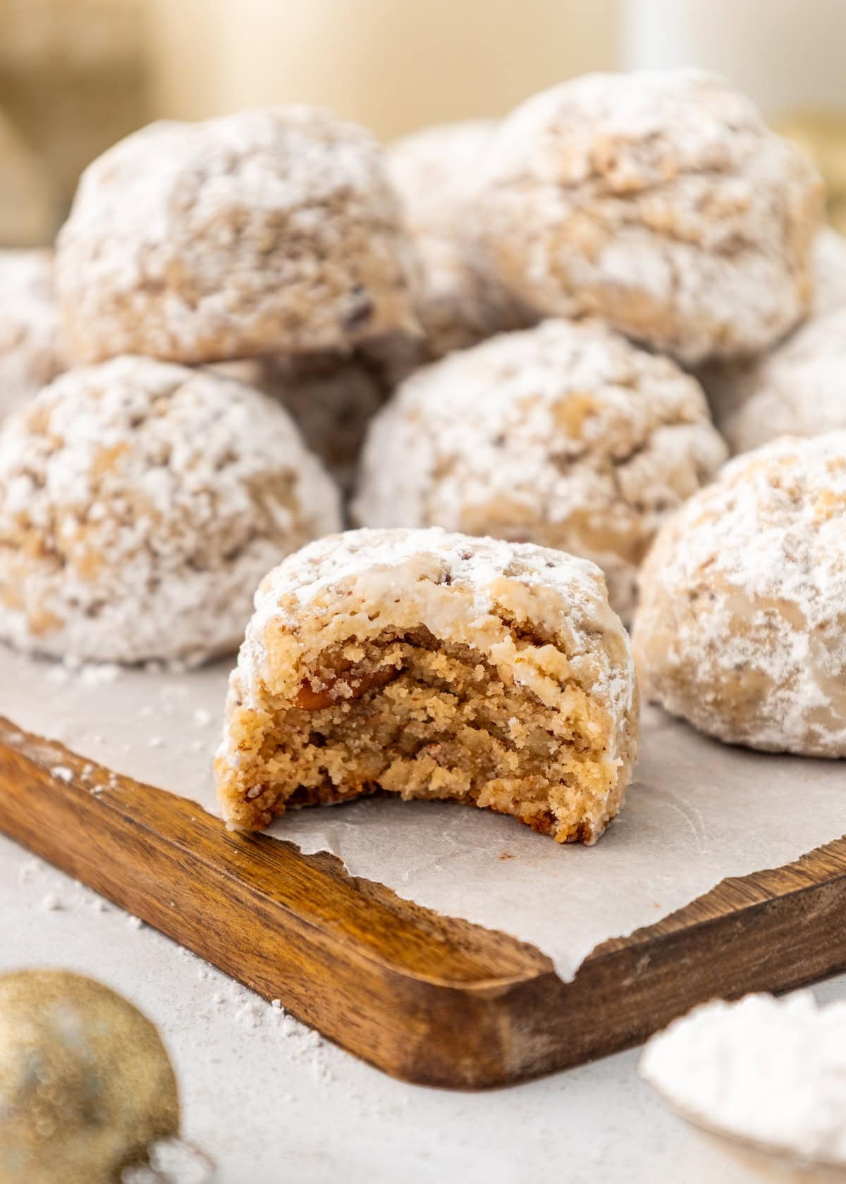 Pecan Snowball Cookies, dusted with powdered sugar, rest on a wooden tray—one has a bite.