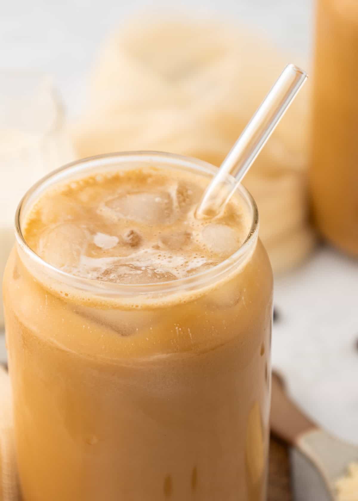 Protein Iced Coffee with a glass straw in a clear glass, filled with ice cubes.