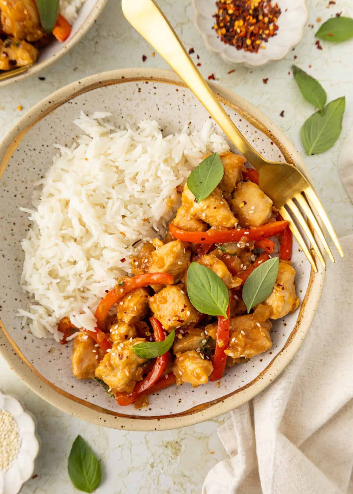 A plate of Thai Basil Chicken with white rice, red bell peppers, and fresh basil leaves.