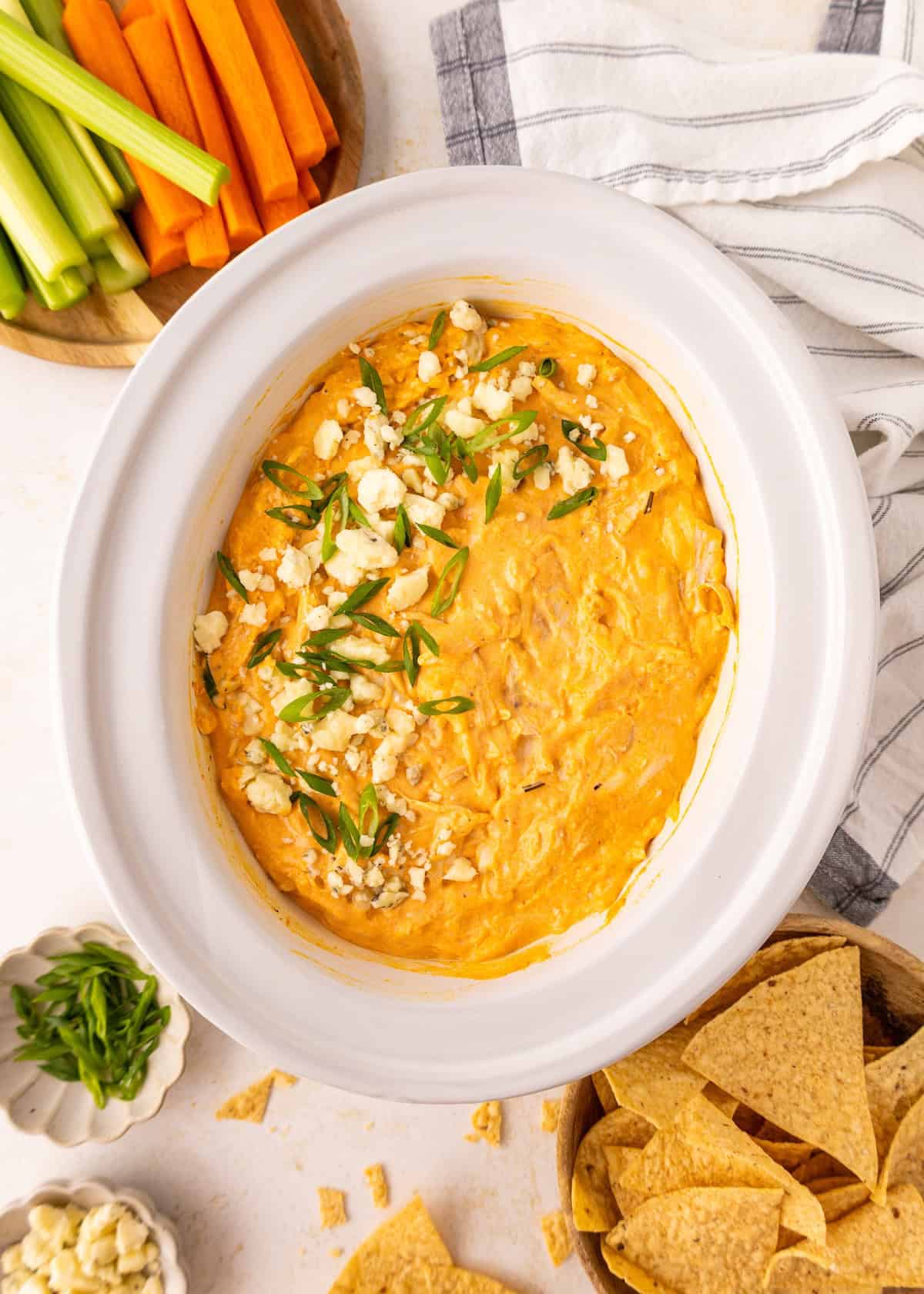 Buffalo chicken dip topped with green onions and cheese, surrounded by chips and veggies.