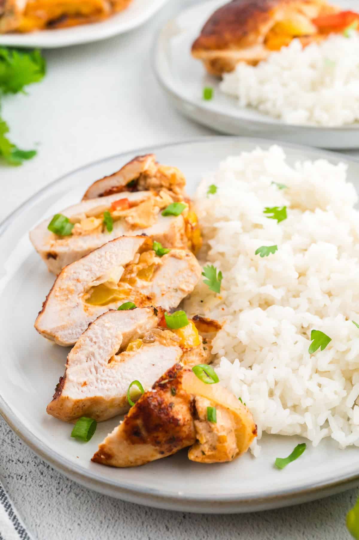 Sliced stuffed chicken breast with white rice, garnished with green onions on a plate.