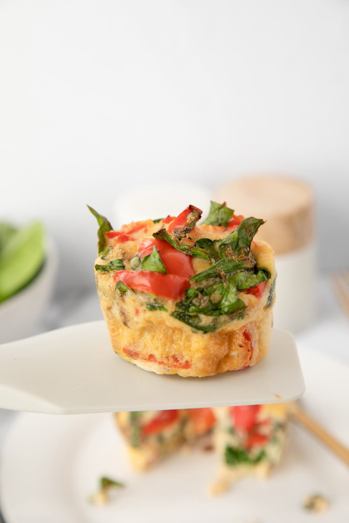 A mini egg muffin with spinach and tomato on a spatula, ready to be served.