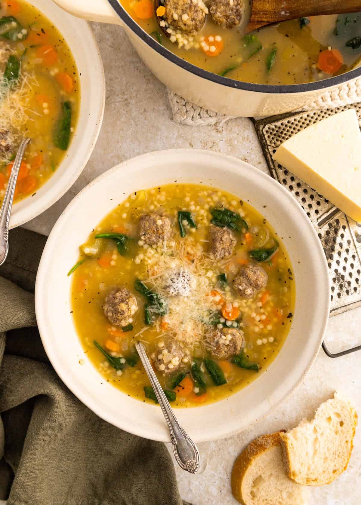 Bowl of Italian Wedding Soup with meatballs, carrots, spinach, and grated cheese on top.