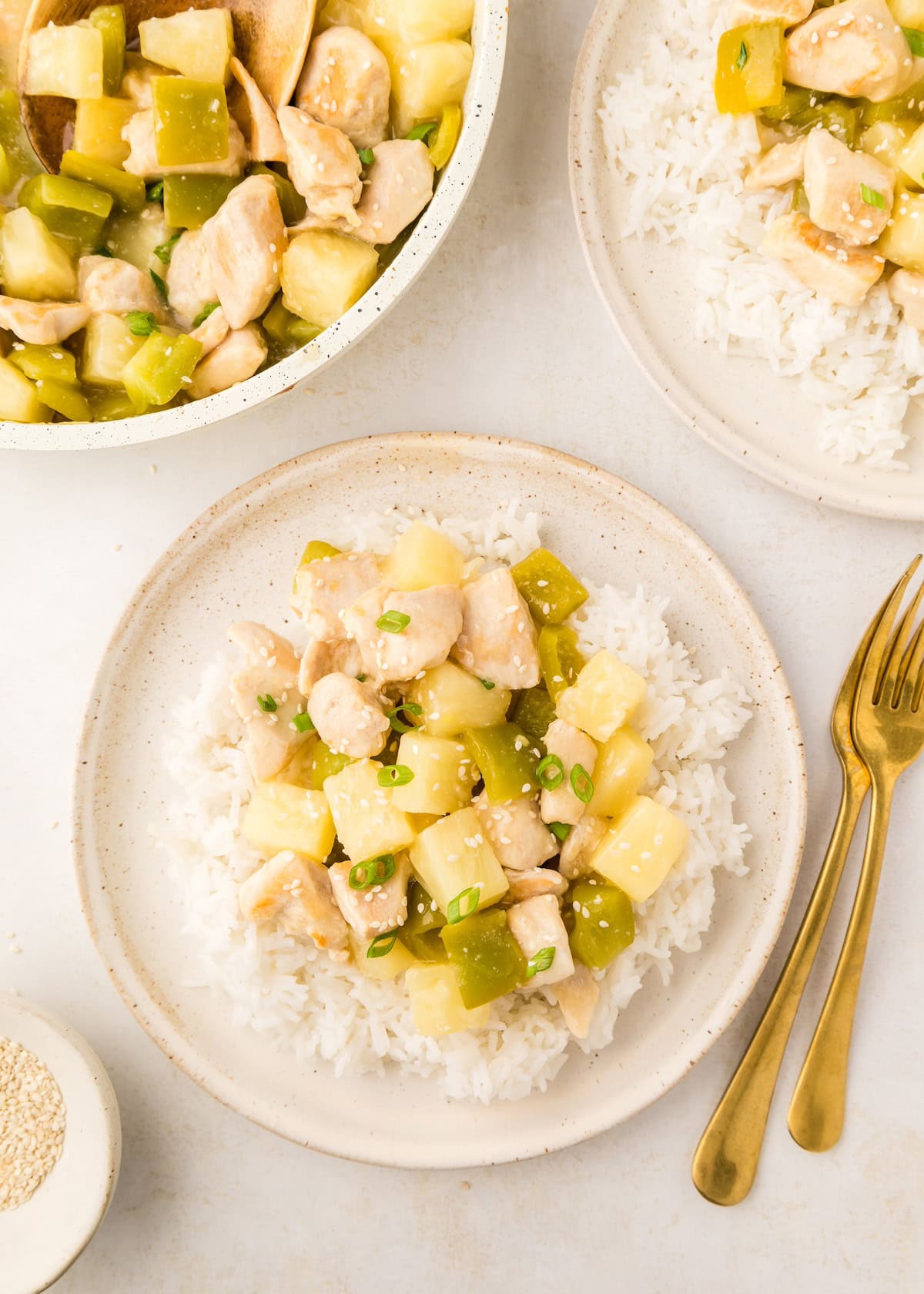 Chicken, pineapple, and green bell pepper stir-fry served over white rice on beige plates.