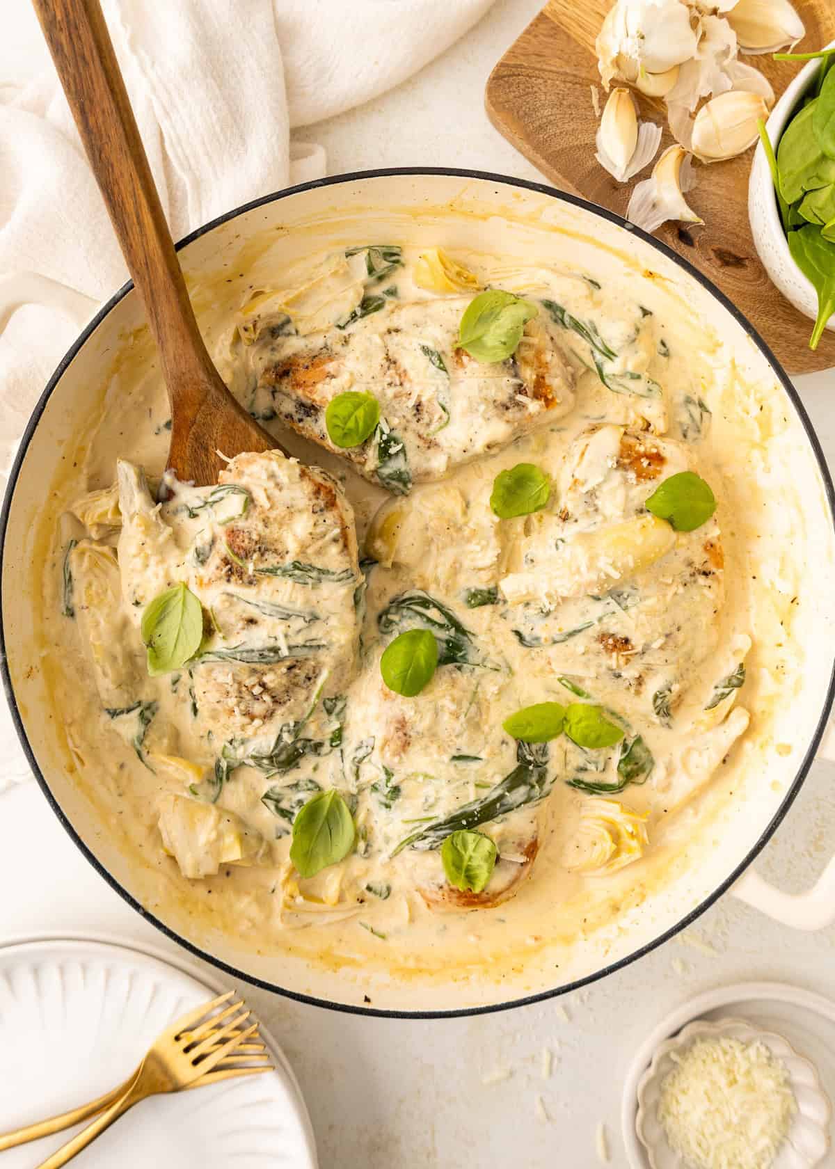 Creamy chicken in a skillet with spinach, basil, and sauce, stirred with a wooden spoon.