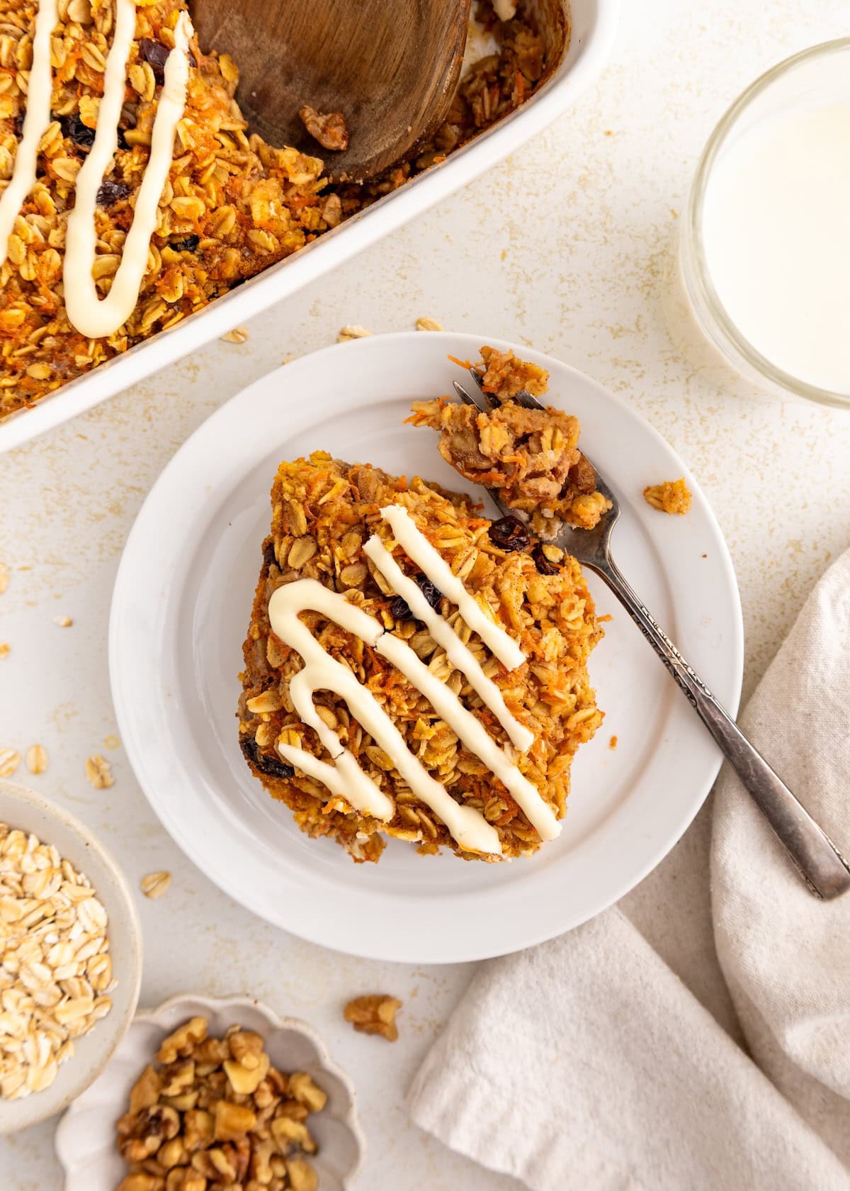 A slice of baked oatmeal with icing on a plate, next to a fork and a glass of milk.