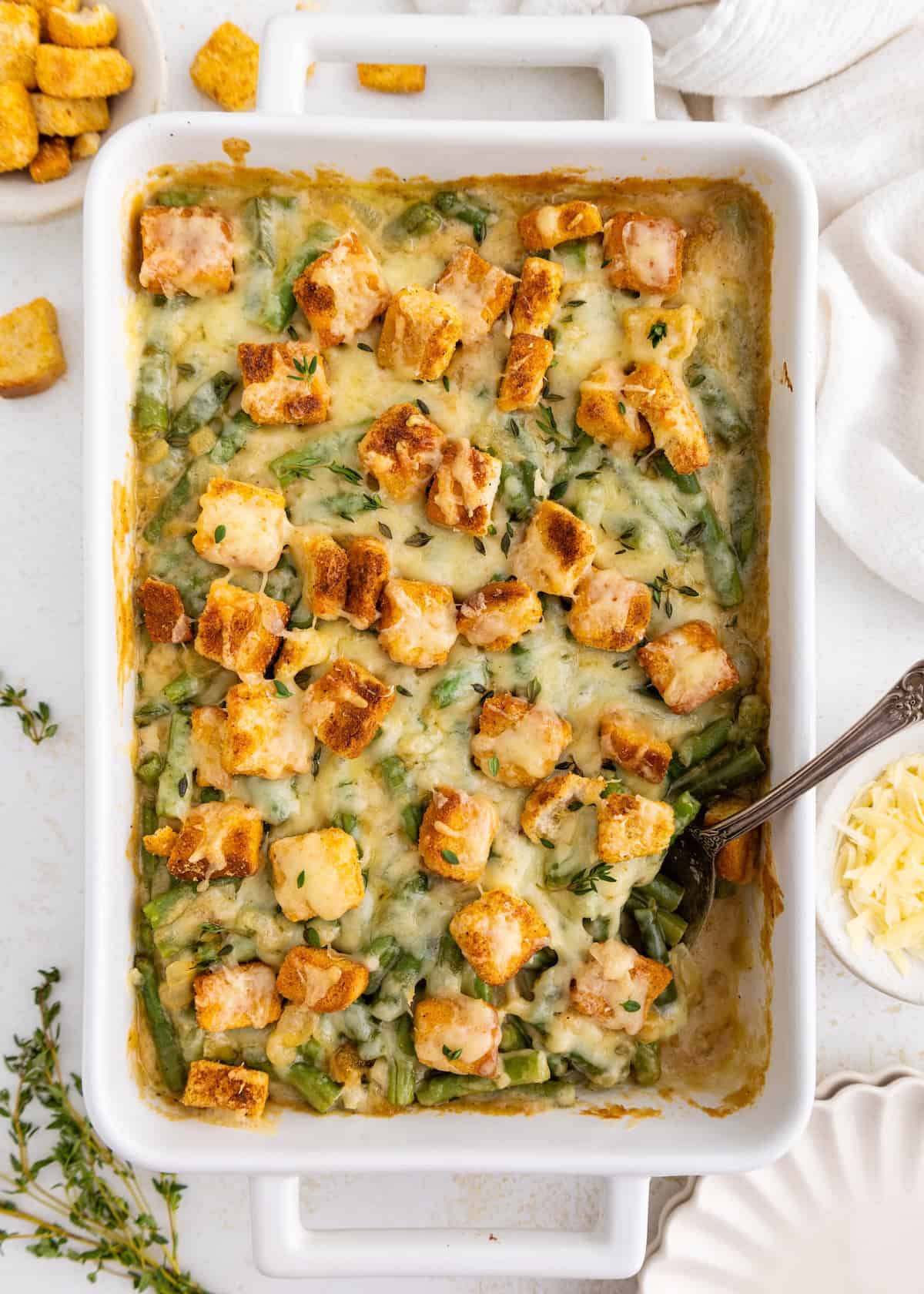 A baked casserole with green beans, cheese, croutons, and chicken pieces in a white dish.