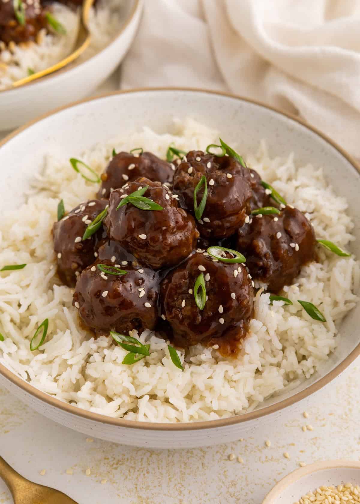 Meatballs with sauce and green onions on white rice, garnished with sesame seeds in a bowl.