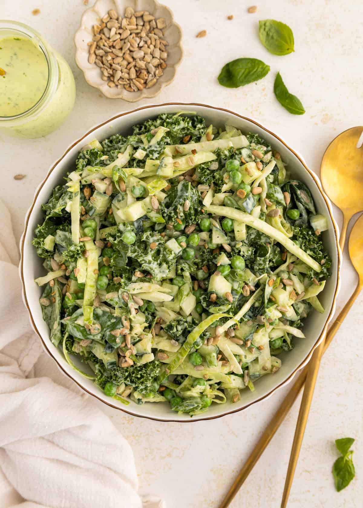 Bowl of green salad with sunflower seeds and creamy dressing, next to gold utensils.