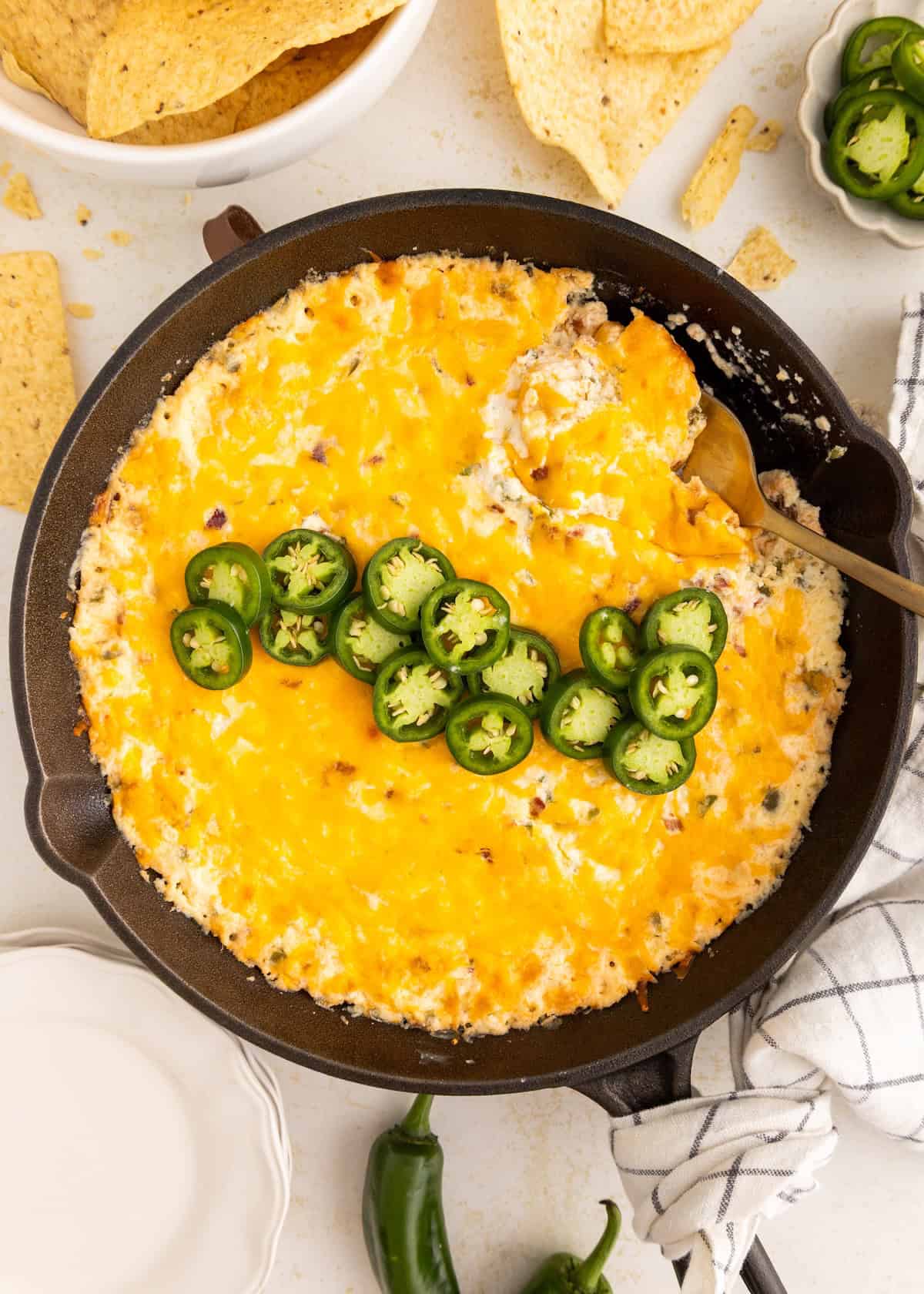 Cheesy baked dip topped with sliced jalapeños in a skillet, surrounded by tortilla chips.