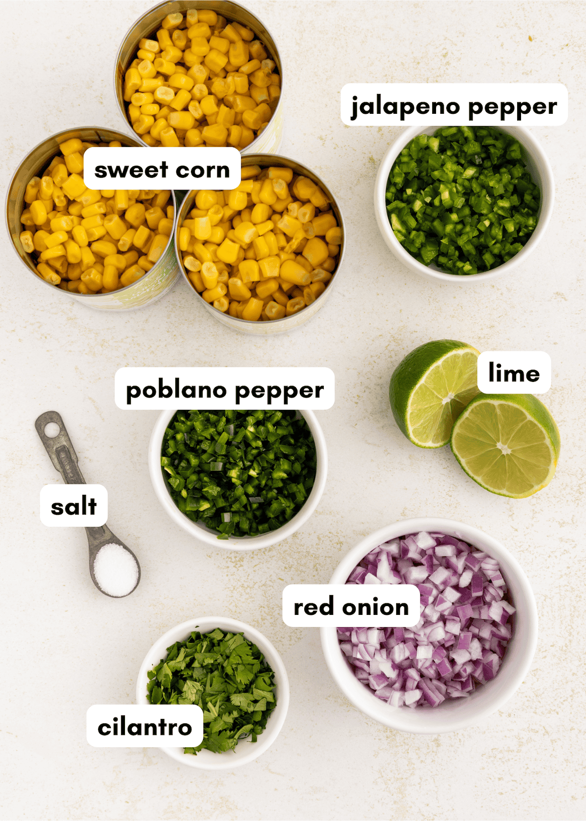 Canned corn, jalapeno, poblano, lime, salt, cilantro, and chopped red onion on a white surface.